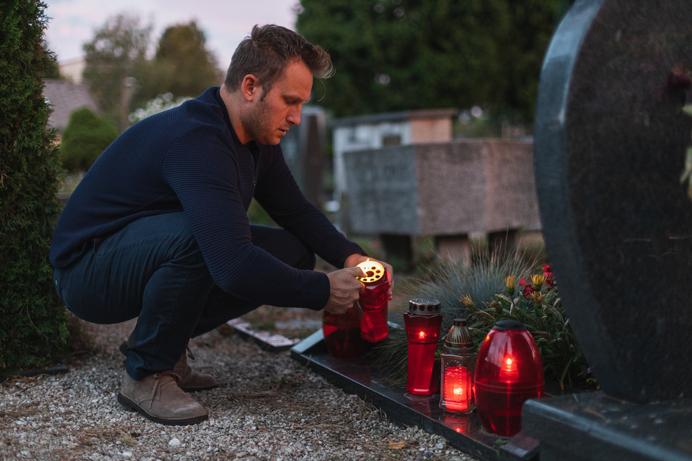 Mann zündet am Friedhof eine Kerze an. 